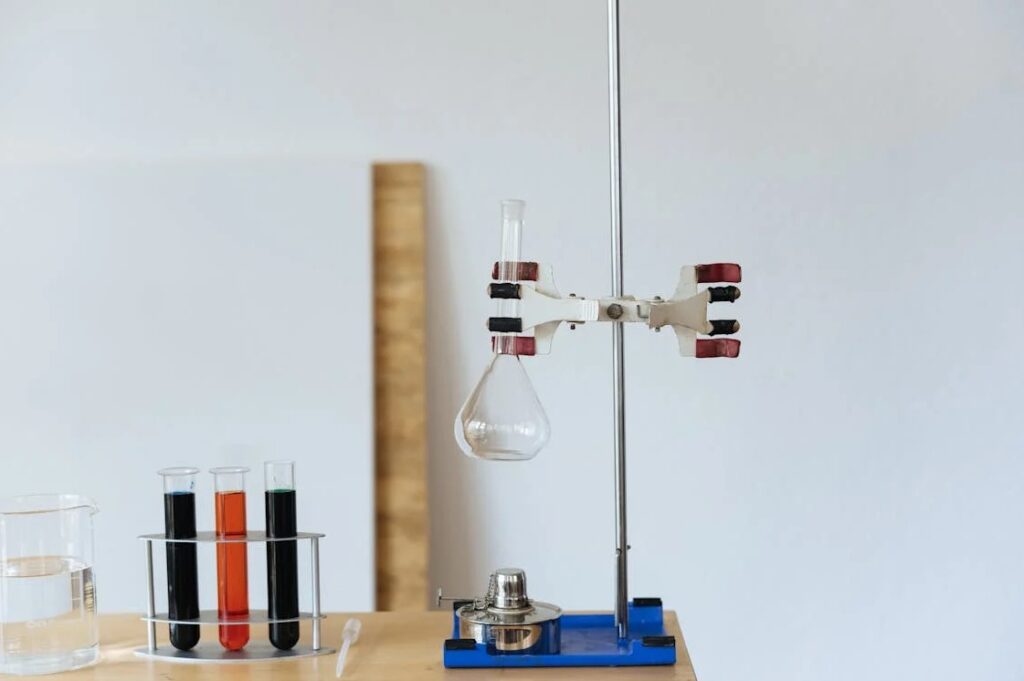 Laboratory bench with test tubes of coloured solution, a beaker, and a flask clamped above a burner on a retort stand